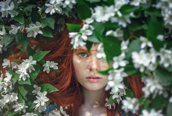 a beautiful girl with red hair looking through a beautiful flower bush - this picture is used in article about omega 3 beauty benefits