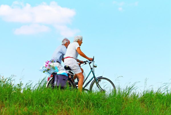elderly man and woman riding bicycles in a field of green grass - this picture is used in article about the benefits of omega 3 for elderly people
