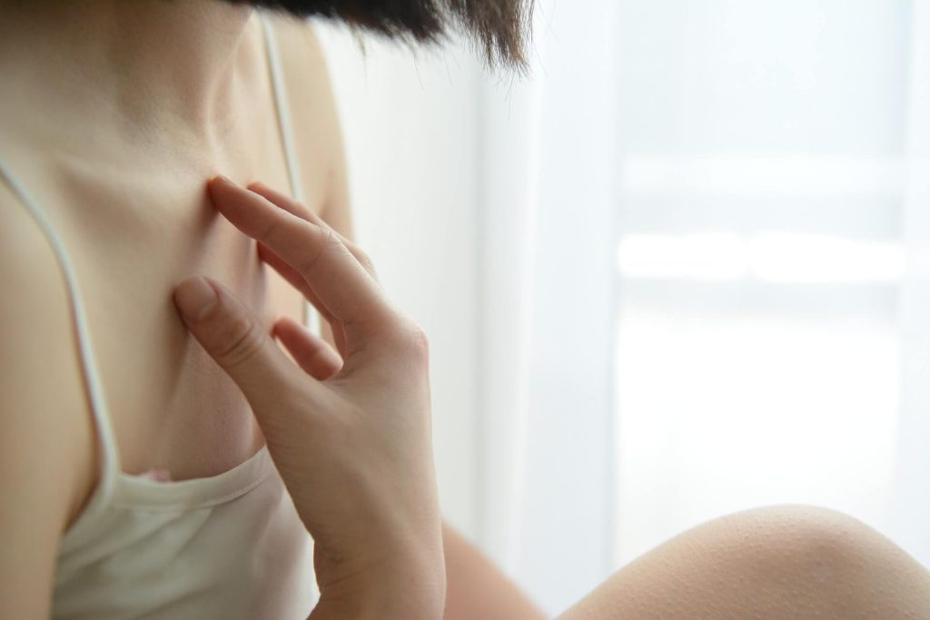 a close up picture of a woman with short hair in a white top touching her chest - this picture is used in article about omega 3 benefits for psoriasis