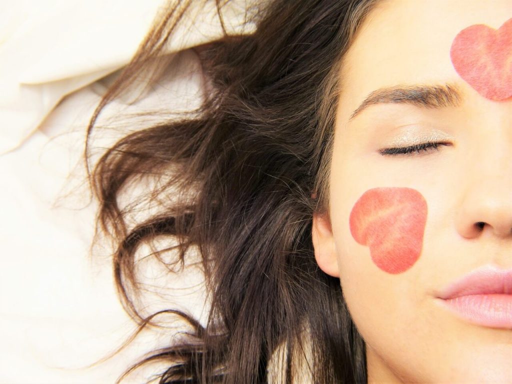woman laying and only her face is seen with closed eyes and rose petals on her cheek and forehead - this piture is used in article about omega 3 benefits for rosacea
