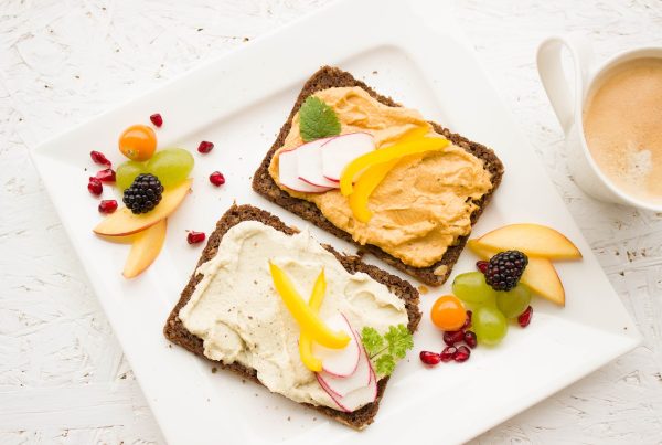 healthy dark bread with humus on top of it and fruits on the side, on a white plate