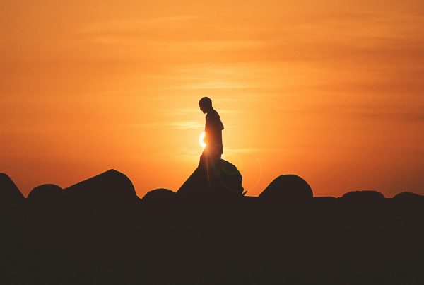 a silhouette of a man walking over rocks in the orange sunset - used in article on fast