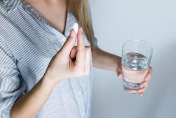 Woman Holding Half-full Glass and White Medicine Pill - used in article on Salbutamol