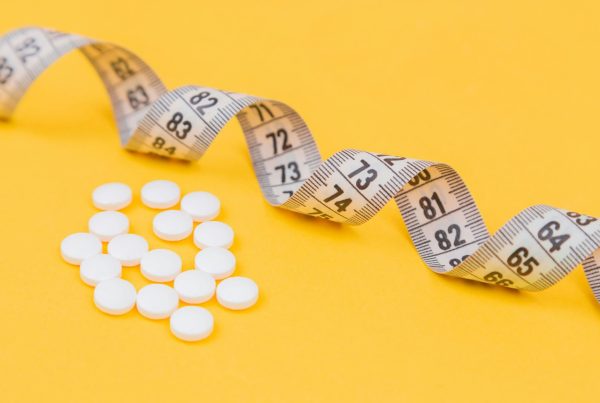 White measuring tape with a white pills used in article on Prescription Medications Obesity