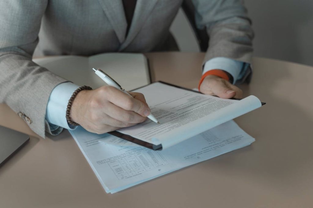 Person in Gray Suit Holding White Pen and Document on a Clipboard - used in article on Importation Medicinal Products Germany