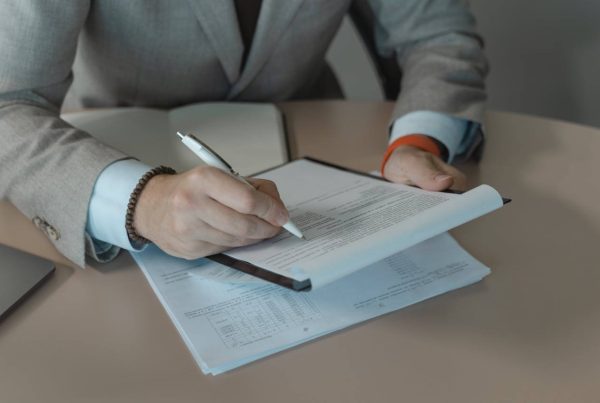 Person in Gray Suit Holding White Pen and Document on a Clipboard - used in article on Importation Medicinal Products Germany